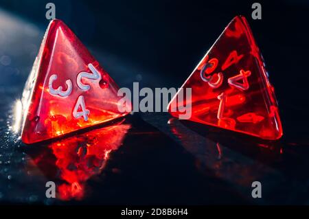 Nahaufnahme von zwei roten 4-seitigen Würfeln auf einer feuchten Schieferfläche. Streulicht Stockfoto