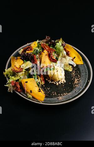 Herbstsalat mit Kürbis und sonnengetrockneten Tomaten auf einem schwarzen Hintergrund Stockfoto
