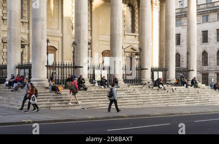 Eine Gruppe von Obdachlosen, die auf den Stufen von St. Martin auf der Fields Church sitzen und am Nachmittag ihr Abendessen essen. London Stockfoto