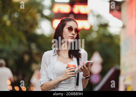 Eine Frau in Sonnenbrillen läuft mit Kaffee auf der Straße. Stockfoto