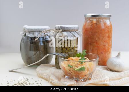 Hausgemachte Gläser mit fermentiertem Kohl, Erbsen, eingelegten Gurken auf hellem Hintergrund, etwas Sauerkraut in einer Glasschüssel Stockfoto