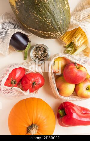 Herbsternte Hintergrund: Bio-Lebensmittel - Melone, Mais, Kürbis, Birne, Äpfel, Granatapfel, Tomaten, Samen in wiederverwendbaren Baumwollnetzbeutel auf cremigem Hintergrund Stockfoto