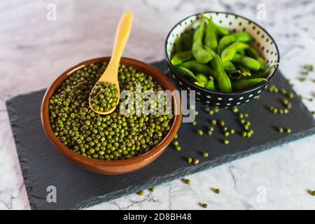 Natürliche edamame Schoten und Mungbohnen in Behältern in der Küche auf einer Marmorplatte Stockfoto