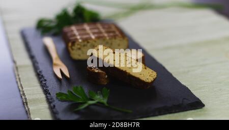 Ein Stück nahrhafte Soja Tempeh in Scheiben geschnitten auf einem Schieferteller mit frischer Petersilie und einer Holzgabel. Stockfoto