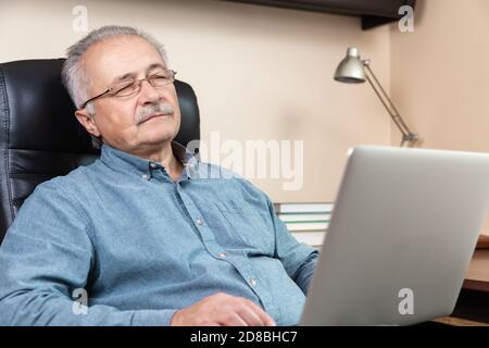 Schlafen Senior Geschäftsmann arbeiten zu Hause. Ein älterer Mann mit Brille arbeitet mit einem Laptop aus der Ferne. Fernarbeit während des Coronovirus-Konzepts Stockfoto