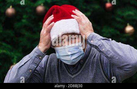 Schockiert oder überrascht Weihnachten. Nahaufnahme Porträt eines älteren Mannes, der einen weihnachtsmannhut und eine medizinische Maske mit Emotionen trägt. Vor dem Hintergrund eines C Stockfoto