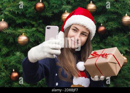 Weihnachten Online-Grüße. Mädchen in weihnachtsmann Hut Gespräche und mit Handy-Smartphone für Video-Anruf Freunde und Eltern. Weihnachten während des Coronavirus Stockfoto