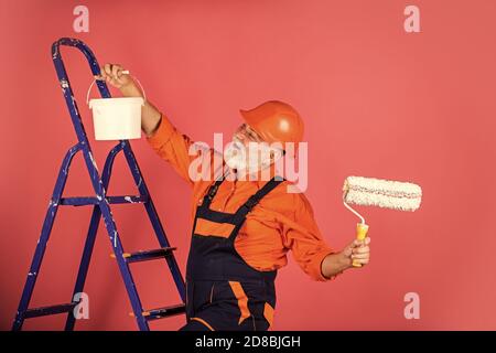 Arbeiten in der Werkstatt. Leitender Maler verwendet Rollen auf Leiter. Wand in Rosa malen. Professioneller Maler in Arbeitskleidung. Arbeiter malen Wand im Zimmer. Malerarbeiten mit Rolle für Männer. Stockfoto