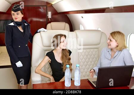 Air Hostess steht in der Nähe sprechende Passagiere von Corporate Jet im Flugzeug. Stockfoto