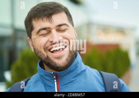 Bärtig lächelnder, fröhlicher junger Mann geht in blauer Jacke im Freien. Stockfoto