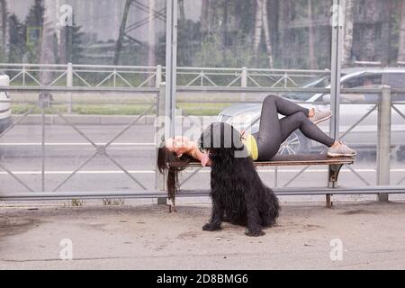 Weiße Frau mit briard in der Nähe liegt auf Bank an der Bushaltestelle. Stockfoto