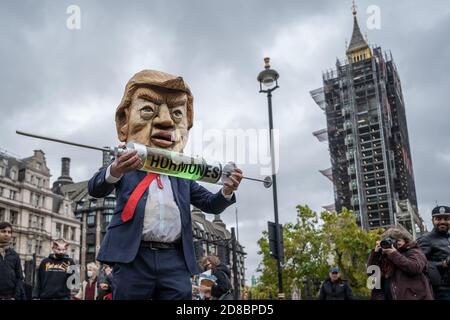 ‘Stop the US Trade Deal’ Protest auf dem Parliament Square mit einer Donald Trump Karikatur, die versucht, eine Pantomime-Kuh mit Wachstumshormonen zu injizieren, Großbritannien. Stockfoto