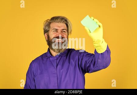 Frühjahrsputz-Service. Verwenden Schwamm für die Reinigung. Ehemann sauberes Haus. Hygiene und Reinheit. Bärtiger Mann tragen Gummihandschuhe. Reife Hausmeister in uniform gelbem Hintergrund. Stockfoto