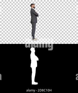 Selbstbewusster Geschäftsmann mit Bart und Mustaschen im Anzug stehend mit gefalteten Händen, Alpha Channel mit Silhouette Stockfoto