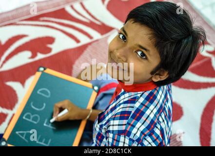 Durgapur/Indien – Oktober 15,2020. Eine hübsche Studentin schreibt Alphabete und lächelt an der Kamera. Selektiver Fokus wird verwendet. Stockfoto