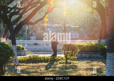 Asiatischer Mann, der im Stadtpark läuft und das Handy benutzt. Fotos mit Unschärfen in Bewegung. Shenzhen, China, 2018-03-09 Stockfoto