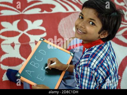 Durgapur/Indien – Oktober 15,2020. Eine hübsche Studentin schreibt Alphabete und lächelt an der Kamera. Selektiver Fokus wird verwendet. Stockfoto