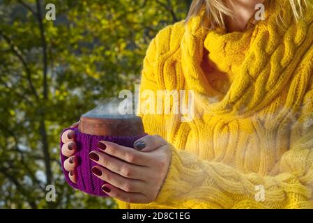 Nahaufnahme der keramischen Tasse heißen Kaffee oder Tee in weiblicher Hand. Heiße Beverege trinken im Herbstpark. Wärmende warme Getränk im Herbstwald Stockfoto