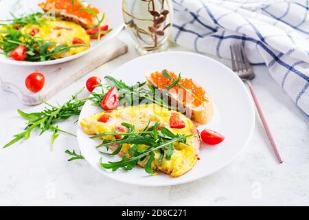 Omelette mit Tomaten, Käse, Schinken und Sandwich mit rotem Cavier auf dem Teller. Frittata: italienisches Omelett. Stockfoto