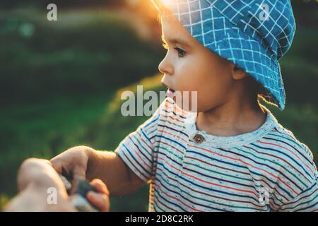 Nahaufnahme Foto von einem kaukasischen kleinen Jungen mit einem Blue hat nimmt etwas von seiner Eltern Hand beim Spielen In einem Feld Stockfoto