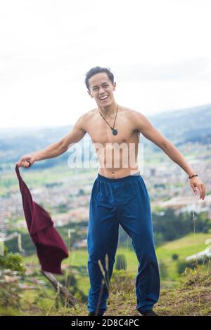 Flacher Fokus eines lächelnden jungen Mannes, der ein abzieht t-Shirt auf einem Hügel Stockfoto