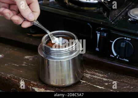 Kaffeemaschine, Kaffee, Löffel und tragbarer Gasherd auf Parkbank. Prozess der Herstellung von natürlichem Kaffee während des Picknicks. Lifestyle. Stockfoto