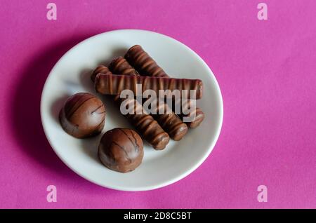 Zufällige Pralinen in weißer Untertasse auf rosa Hintergrund. Portion Konditorei. Süße Leckereien. Selektiver Fokus. Stockfoto