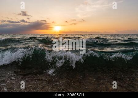 Eine Welle stürzt in die Meeresküste als die Sonne Setzt sich in den bunten Sonnenuntergang Himmel Stockfoto