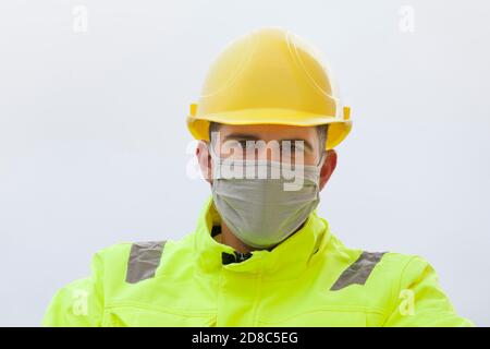 Portrait von lächelnden jungen Ingenieur mit Gesichtsmaske und hart mütze und Arbeitsschutzkleidung Stockfoto