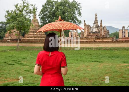 Die Landschaft einer Frau mit ihrem Lanna-Regenschirm, der an einem bewölkten Tag in der Regenzeit in der Provinz Sukhothai, Thailan im Tempel Wat Mahathat spazieren geht Stockfoto