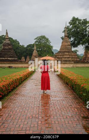 Die Landschaft einer Frau mit ihrem Lanna-Regenschirm, der an einem bewölkten Tag in der Regenzeit in der Provinz Sukhothai, Thailan im Tempel Wat Mahathat spazieren geht Stockfoto