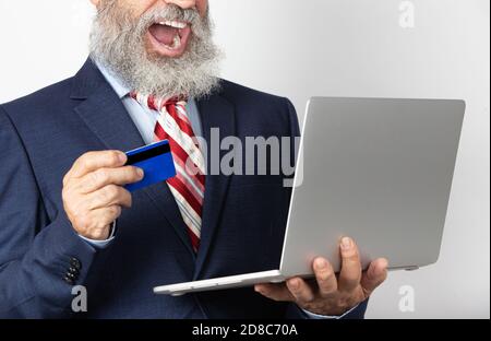 Aufgeregt reifen Mann in Anzug mit einer Kreditkarte mit Online-Laptop-Kauf. Leitender Mann mit Technologie auf weißem Hintergrund. Stockfoto