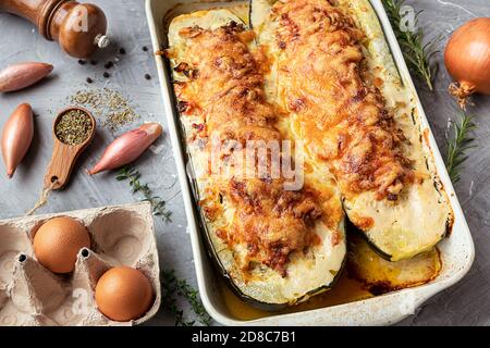 Hausgemachte gefüllte Zucchini, gebacken mit Fleisch, Zwiebeln, Eschalot, Knoblauch, Eier, Kräuter und Käse auf dem grauen Hintergrund Stockfoto