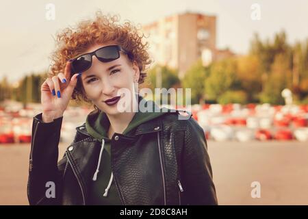 Junge Frau mit afro Frisur mit violetten Lippen in der Stadt. Mädchen tragen lässige Kleidung posiert auf Rennbahn Hintergrund Stockfoto