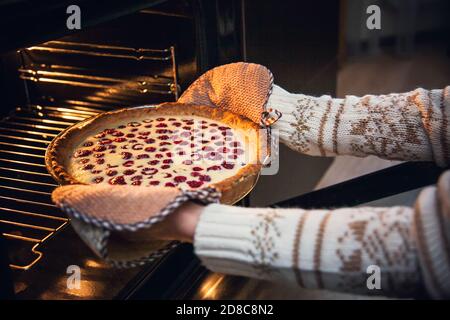 Frau im Weihnachtspullover nimmt Himbeer-Shortcake aus dem Ofen. Stockfoto