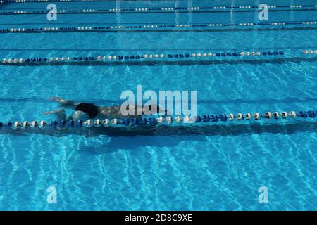 Unerkennbarer Mann mittleren Alters beim Schwimmen und Tauchen im Freibad. Rückansicht eines Mannes unter Wasser. Sport und aktiver Lebensstil im mittleren Alter. Stockfoto