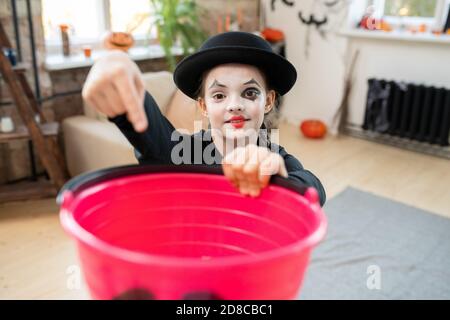 Portrait von lächelnden Pantomime Mädchen mit Herz auf Lippen gezeichnet Zeigt in Eimer und bittet, Halloween Süßigkeiten zu setzen Stockfoto