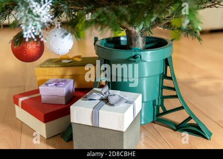 Geschenkboxen stehen in der Nähe eines Kunststoff-Weihnachtsbaum stehen in Form eines Eimers zu Hause in Silvester auf dem Boden in der Stadt Wohnung. Stockfoto