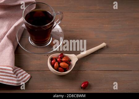 Eine Tasse Vitamintee mit Hagebutte und einen Holzlöffel mit Früchten. Natürlicher Kräutertee. Horizontale Ausrichtung Stockfoto