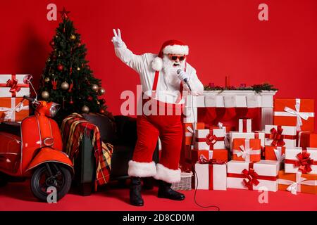 Foto in voller Länge von verrückten weihnachtsmann singen Lied in MIC isoliert auf rot hellen Hintergrund mit Weihnachten Kamin Geschenkbox Stuhl Stockfoto