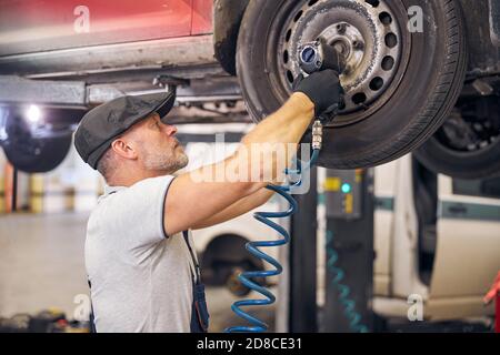 Bärtige Auto Mechaniker Reparatur Auto Rad Scheibe in der Garage Stockfoto