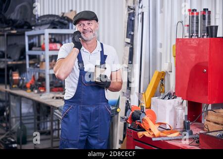 Fröhlicher Mechaniker, der in der Garage am Handy spricht Stockfoto