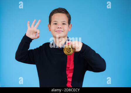 Schöner Junge zeigt seine goldene Medaille auf blauem Hintergrund. Stockfoto