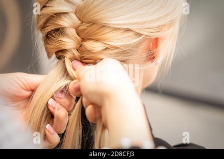 Nahaufnahme der Rückansicht der weiblichen Hände, die ein Zopf umflechten An junge blonde Frau im Schönheitssalon Stockfoto