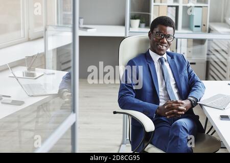 Porträt eines erfolgreichen afrikanischen Geschäftsmannes, der während des Sitzens die Kamera anlächelt Auf dem Stuhl im Büro Stockfoto
