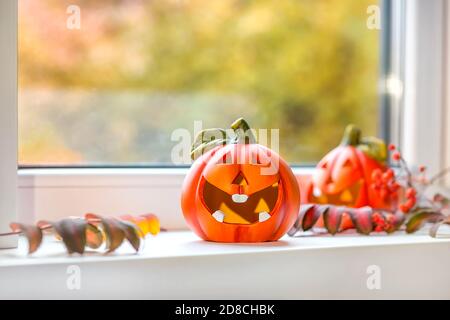 Lustige Deko-Kürbisse für Halloween stehen auf der Fensterbank. Vor dem Fenster, Herbstlandschaft, Bokeh. Selektiver Fokus. Stockfoto