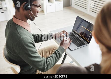 Afrikanischer Mann im Kopfhörer, der auf Laptop schreibt und spricht Arbeiten im Kundendienst Stockfoto