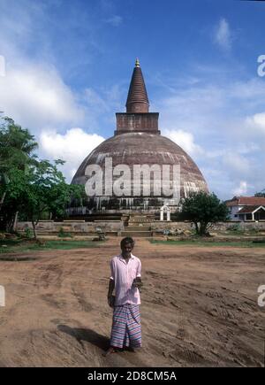 Ein Souvenirverkäufer steht vor Jetavanaramaya Dagoba ist ein Stupa, oder buddhistische Reliquiendenkmal, in den Ruinen des Jetavana Klosters in der alten buddhistischen Heiligen Stadt Anuradhapura, Sri Lanka Stockfoto