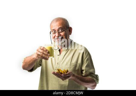 Älterer asiatischer indischer Mann, der Kurkuma-Milch hält oder trinkt Ein Glas - gesunde Ernährung Konzept Stockfoto