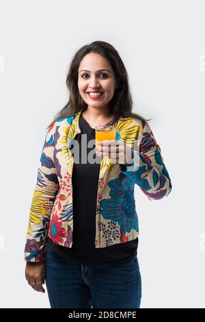 Indische asiatische junge Frau oder Mädchen trinken frischen Orangensaft In einem Glas vor weißem Hintergrund stehen Stockfoto